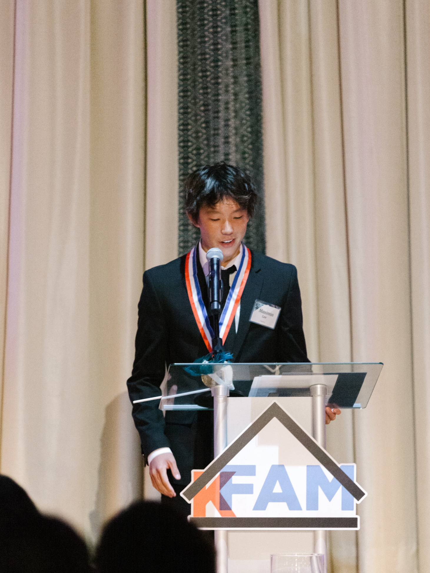 Maximus Lee speaking at a KFAM event podium